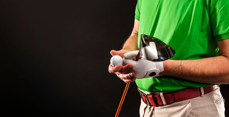 Closeup of a male golfer holding a golf ball, a golf iron and wearing a white golf glove. Horizontal format over a black background.