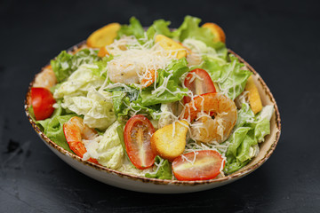 Caesar salad with shrimp in a bowl on a black background.