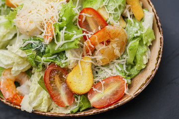 Caesar salad with shrimp in a bowl on a black background.