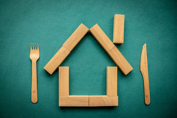 Eco-friendly house made of wooden blocks with wooden knife and fork on a blue background. Planet care concept. Flat lay, top view, copy space.