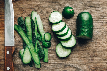 Sliced fresh green cucumbers with a knife on a wooden background. Top view. Copy, empty space for text