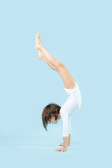 Fit little girl in a white leotard doing handstand over blue background