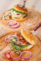 Delicious juicy burgers. Beef patty with toasted bun, salad and onions. Serving on wooden boards on the restaurant table. Fast food restaurant menu.