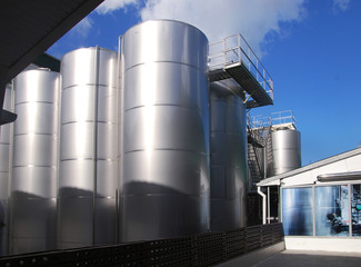 Large metallic glossy tanks with an observation deck at an outdoor plant on a sunny day