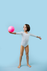 Little girl in a white leotard with gymnastic ball over blue