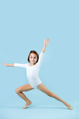 Fototapeta na wymiar Artistic little girl in a white leotard doing gymnastic form over blue
