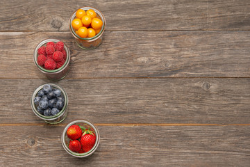 different types of berries in small glasses on the left side on a wooden table