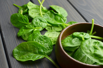 Bowl with fresh green spinach leaves over dark wooden table background. Vegan food trend. Eco-conscious concept.
