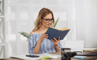 Young girl student sitting at home in the office using book and laptop studing online
