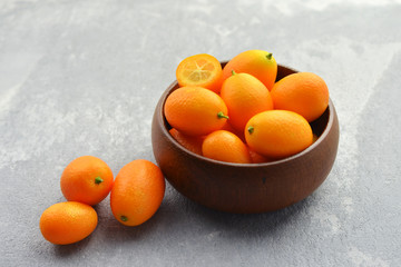 Fresh kumquats in wooden bowl on grey background. Healthy vegan food. Side view.