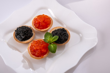 Tartlets and sandwiches with red salmon caviar and black sturgeon  caviar on plate with fresh lemon, ice cube, mint. Healthy diet. Selective focus Copy space Space for text