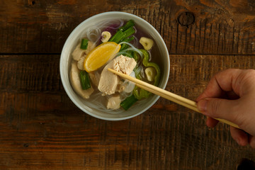 Light plate of Vietnamese Pho soup with chicken on a wooden table with a spoon.