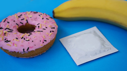 Banana, donut and condom. Sex idea. Bright picture on a blue background. The concept of health and protected sex