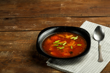Black dish of italian tomato soup with potatoes and mushrooms on a wooden table on a napkin and a spoon.