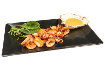 Gourmet squid decorated with sauce and arugula on a black stone plate, isolated on white background
