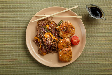Buckwheat soba noodles with vegetables and chicken chop in an Asian style on a bamboo mat.