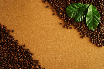 Coffee beans on brown cork background. Fresh green coffee leaves. Frame of brown coffee beans. Space for your text.