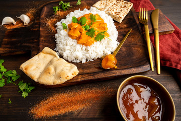 Indian Chicken tikka masala tandoori with naan bread and rice on a rustic wooden plate. Styled with coriander mangoo chutney, garlic and spices. India and food photography concept.