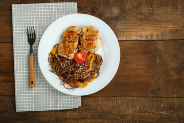 Soba buckwheat noodles with vegetables and chicken chop in a white plate on a linen napkin.