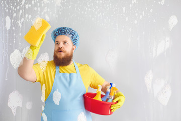 Funny fat man with a beard in an apron washing cleans up on a gray background.