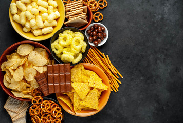 Unhealthy food. pretzels
different chips, crackers, chicolad, cookies in bowls. junk food for a figure, heart, skin, teeth. An assortment of fast carbohydrate foods. with copy space for your text