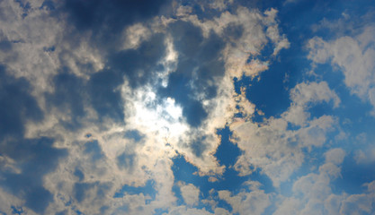 Stormy white clouds on blue sky and sun behind clouds