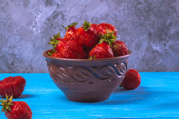 Ripe strawberries in a ceramic brown bowl on a blue background