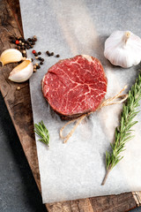 Raw beef filet Mignon steak on a wooden Board on paper with ingredients for grilling