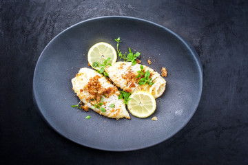 Gebratene Tintenfisch Tuben in Semmelbrösel Panade mit Zitronen Scheibe und Kräuter angboten als Draufsicht auf einem Modern Design Teller © HLPhoto