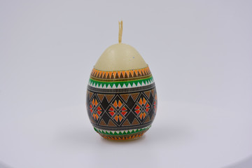 White wax candle in the form of an Easter egg decorated with painting and is located on a white background.