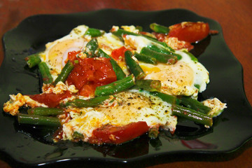 Morning roasted whole eggs on the black plate and with tomato and green beans