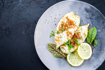 Fried calamari tubes in breadcrumbs breading with lemon slices and lettuce leaves offered as top view on a modern design plate with copy space left