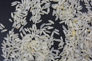 White steamed long-grain rice scattered on a black surface. Healthy and healthy food, rice groats.