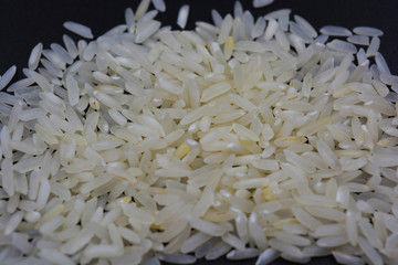 White steamed long-grain rice scattered on a black surface. Healthy and healthy food, rice groats.