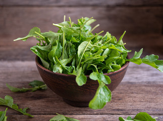 Fresh, ripe arugula in a clay bowl on a wooden table.