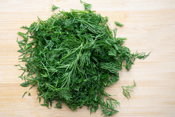 Close-up top view of chopped fresh green dill, cut dill on wooden board in kitchen