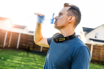 Workout in the backyard. A guy is drinking water from sports bottle in a break of training