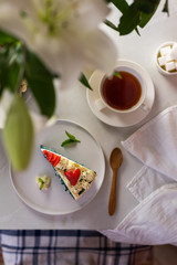 A sliced piece of Blue Velvet cake decorated with cream flowers and a strawberry heart. Tea party for one person. Festive table with a bouquet of Lilies. Vertical flat lay in bright key.