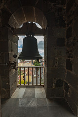 Fototapeta premium Top view through the slatted window from the high tower of the church. Outside the window are tiled roofs of historic buildings. Silhouette of a church bell in a window. La Laguna, Tenerife