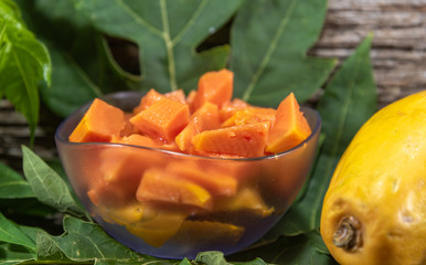 Papaya (Carica papaya L.) chopped in bowl and fresh fruit among papaya leaves
