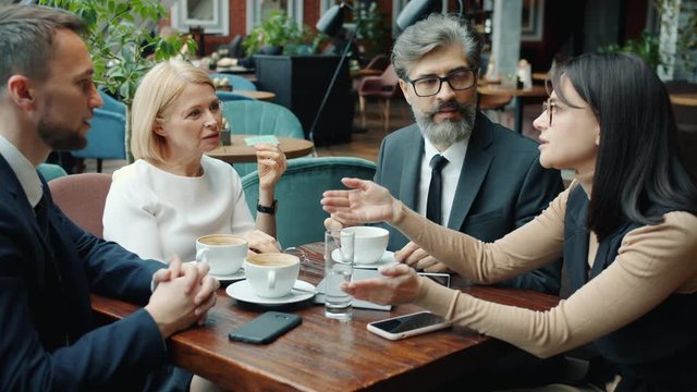 Colleagues men and women are talking in cafe during business lunch discussing work sitting around table together. Conversation and lifestyle concept.