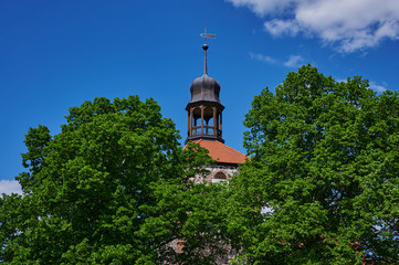 View to the tower of a medieval village church in the state of Brandenburg, Germany, that can be seen through trees.