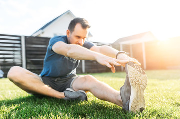 Athletic guy is doing stretching and warming up before a workout outdoors. Sports training in the backyard. Healthy lifestyle concept