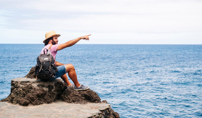 A tourist man with hat and backpack on a rock on the coast with the sea in the background. El Hierro, Canary Islands