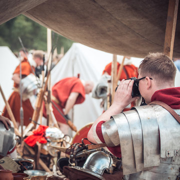 A man in armor of a Roman legionnaire warrior photographs his friends at a festival of reenactors