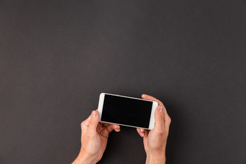 Male hands holding white smartphone in landscape mode on abstract black background with copy space
