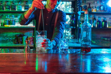 Professional barman finishes preparation of alcoholic cocktail for guest in multicolored neon...