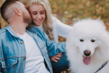 Man and woman with samoyed breed puppy are kissing outdoors