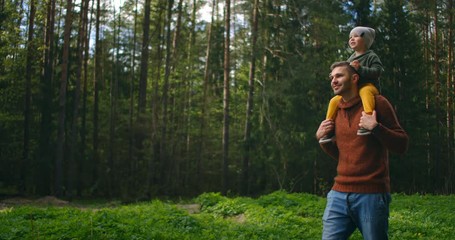Slow motion: Son sitting on his fathers neck in the spring sunny park. Fathers day. Father and boy walk in forest and son on his neck. Father and son went on a forest adventure together.