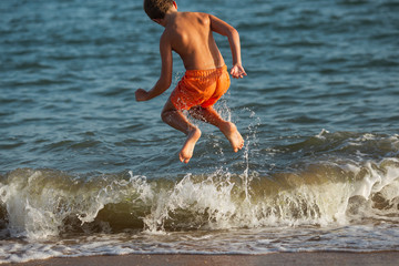 Chico saltando sobre olas en la playa en verano 